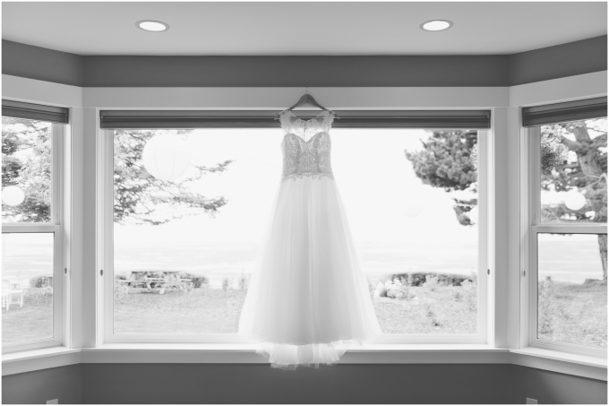Black and white photo of wedding dress hanging in front of a window