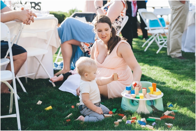 A toddler enjoys playing with building blocks on the lawn at a backyard beach wedding 