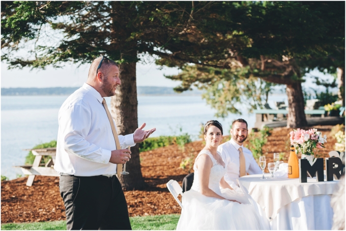 Best man giving his speech at a backyard beach wedding while the bride and groom look at her